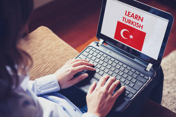 Woman sitting at home with a laptop on the knees and a website to learn Turkish on the screen.